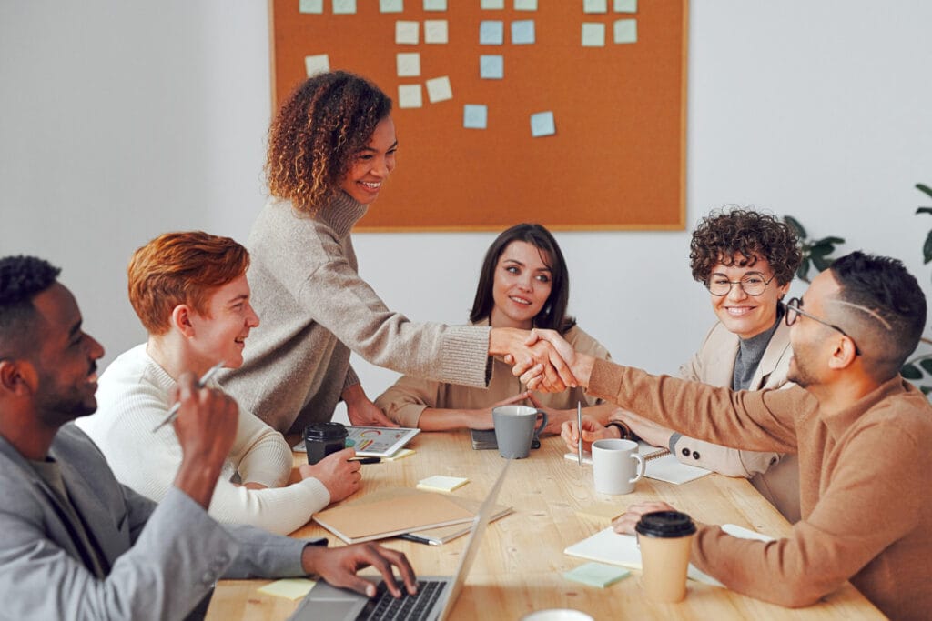 Woman demonstrating emotional intelligence through a collaborative handshake during a workplace meeting. Image @Canva