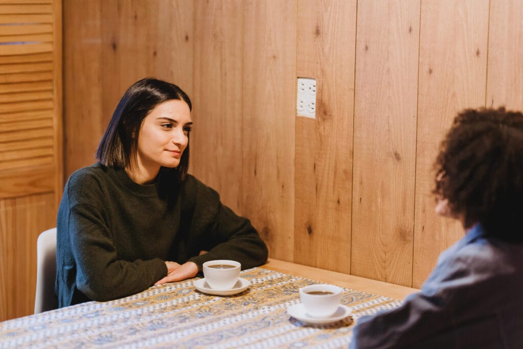 Two people at a table with coffee cups, engaged in conversation. One person pays attentive attention. Image by Liza Summer @Pexels